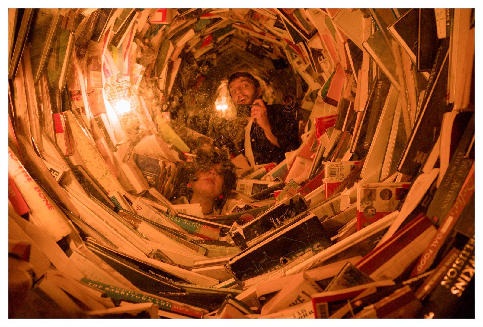 Karen y JP reflejados en una instalación circular de libros